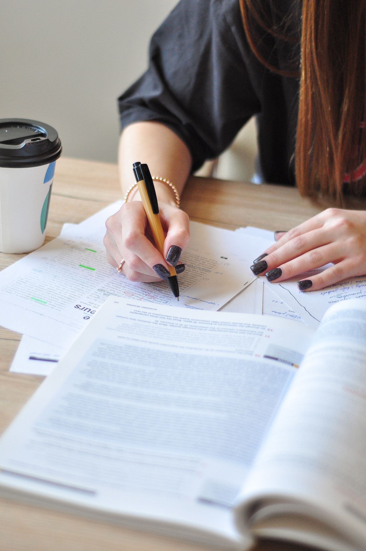 A young woman studying with a pen and coffee cup, focusing on her notes.