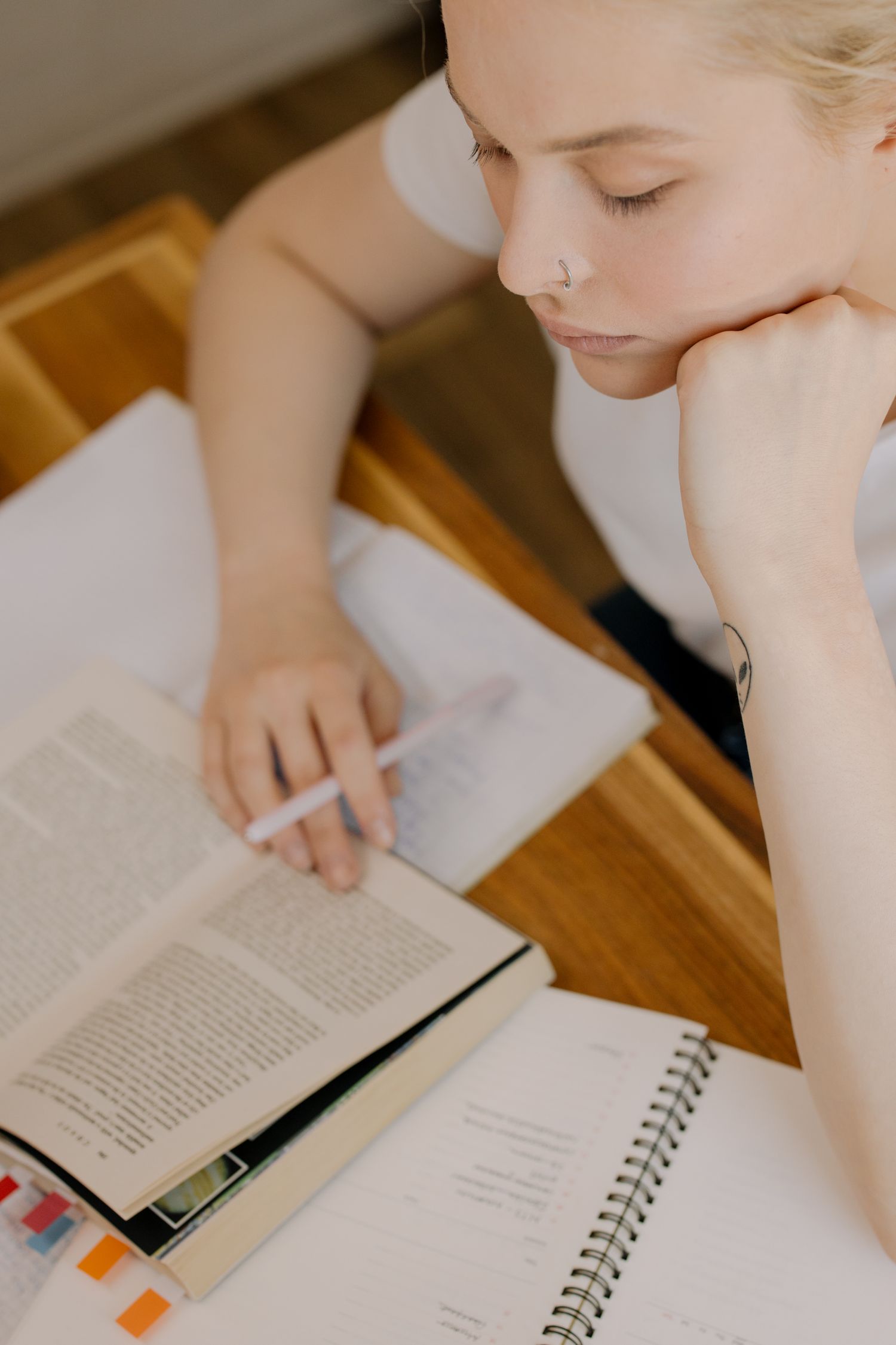 Focused young woman in casual attire studying with open books and notes at a desk.