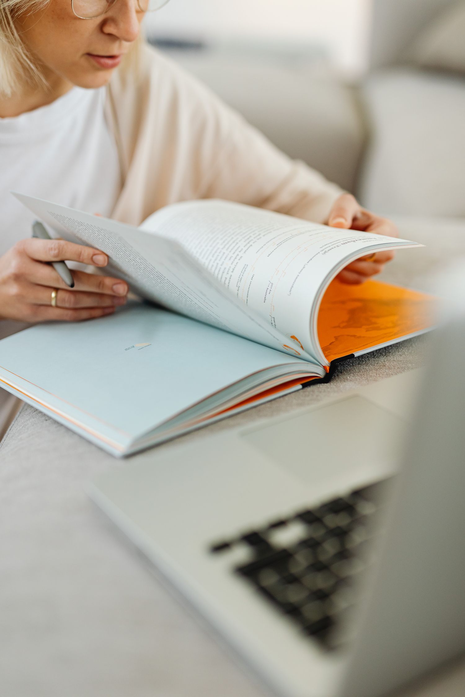 Focused woman studying with book and laptop indoors, depicting modern learning environment.