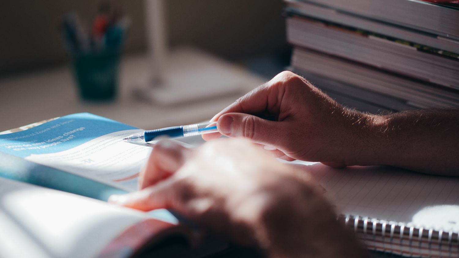 Close-up of hands writing in a notebook with a pen on a desk, suggesting focus and learning.