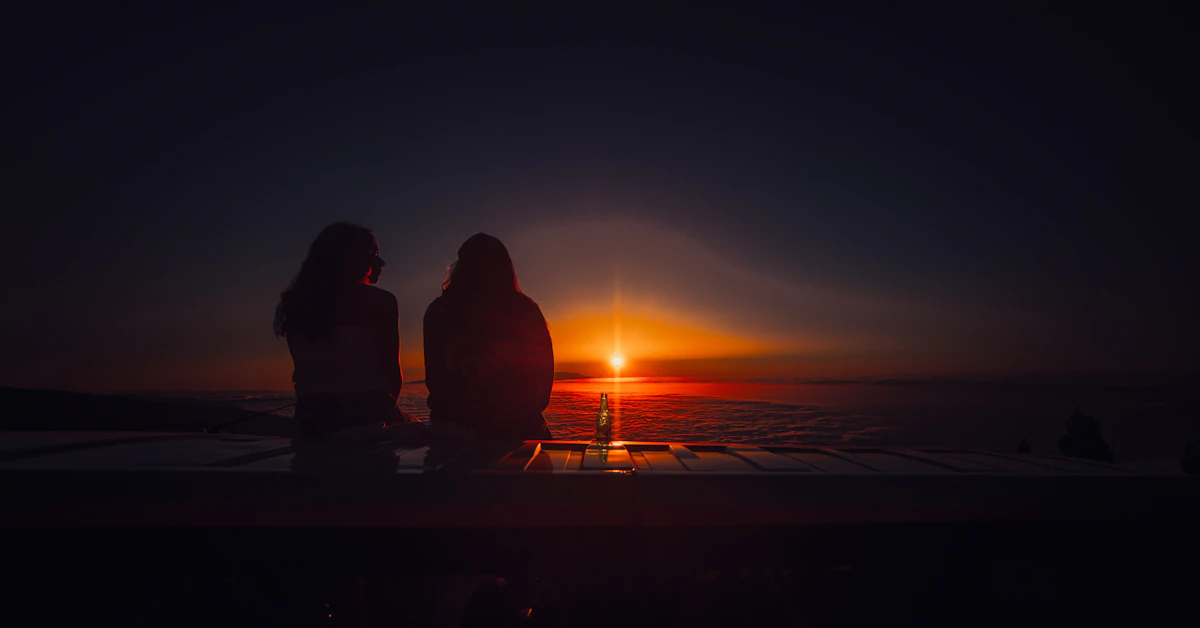 silhouette of 2 person sitting on the edge of the building during sunset