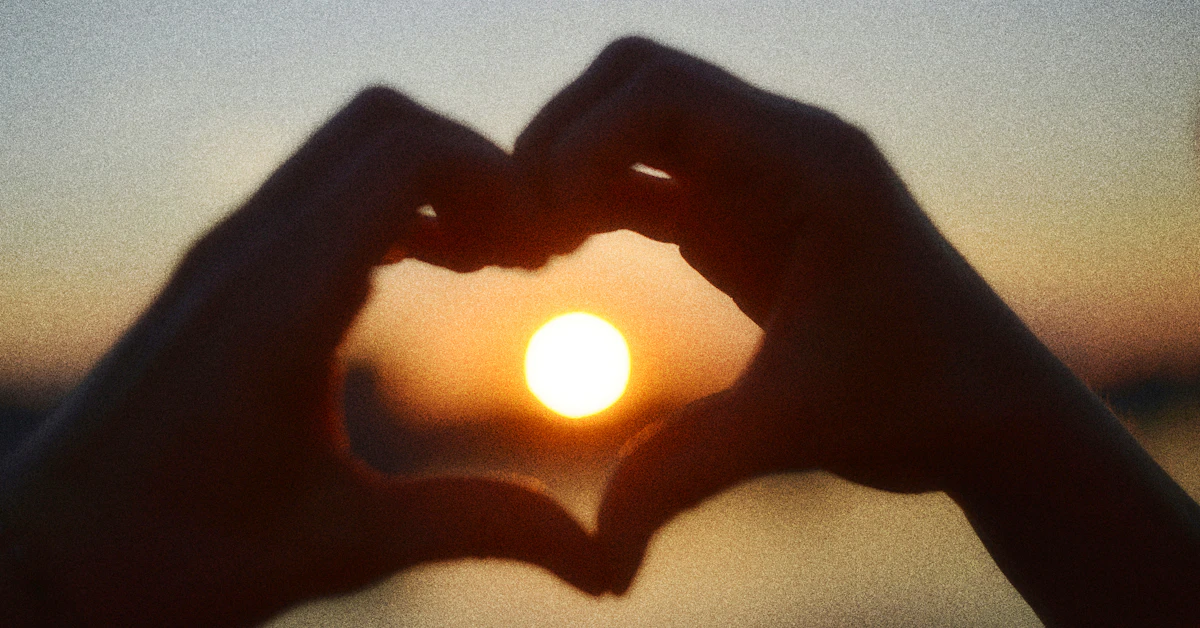 Hands forming a heart shape silhouetted against a beautiful sunset